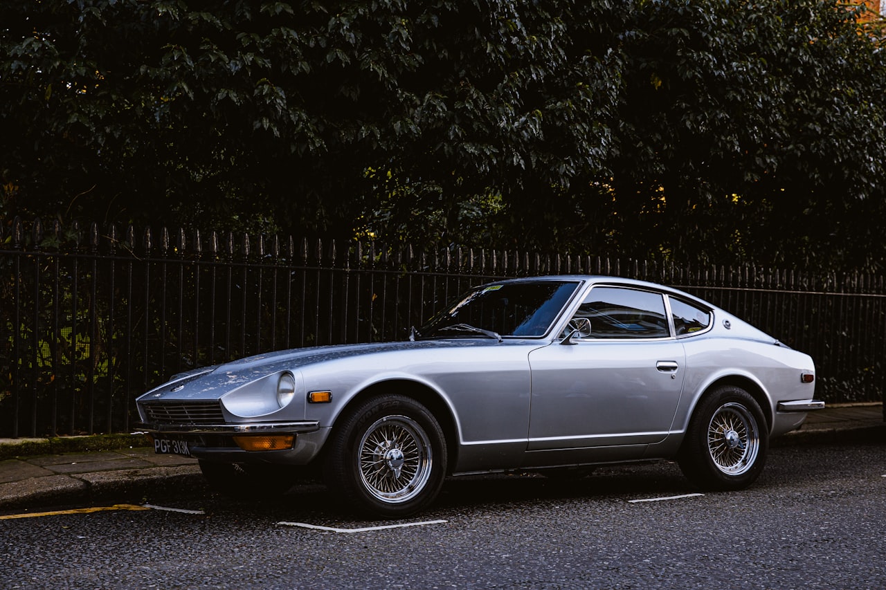 Silver Datsun 240Z parked under trees, showing the elegant coupe body lines