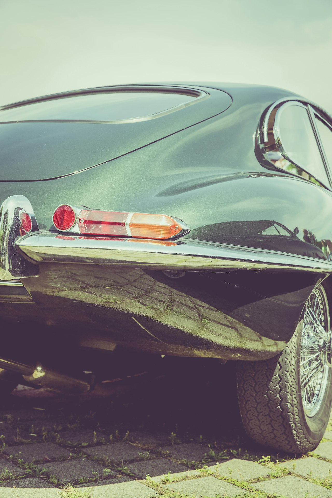 Rear quarter view of a dark green Jaguar E-Type Fixed Head Coupe showing the iconic fastback roofline, tail lights, and wire wheels
