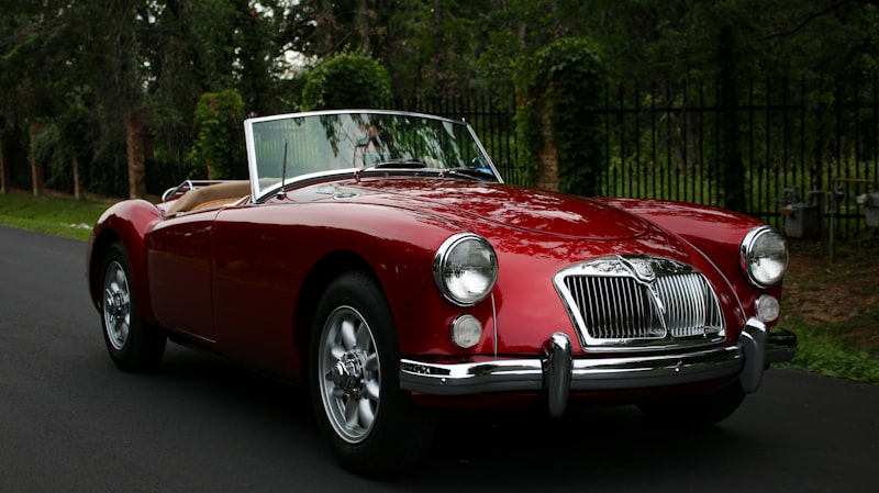 Red MGA sports car driving on a road, showing the classic coupe body shape and rear window