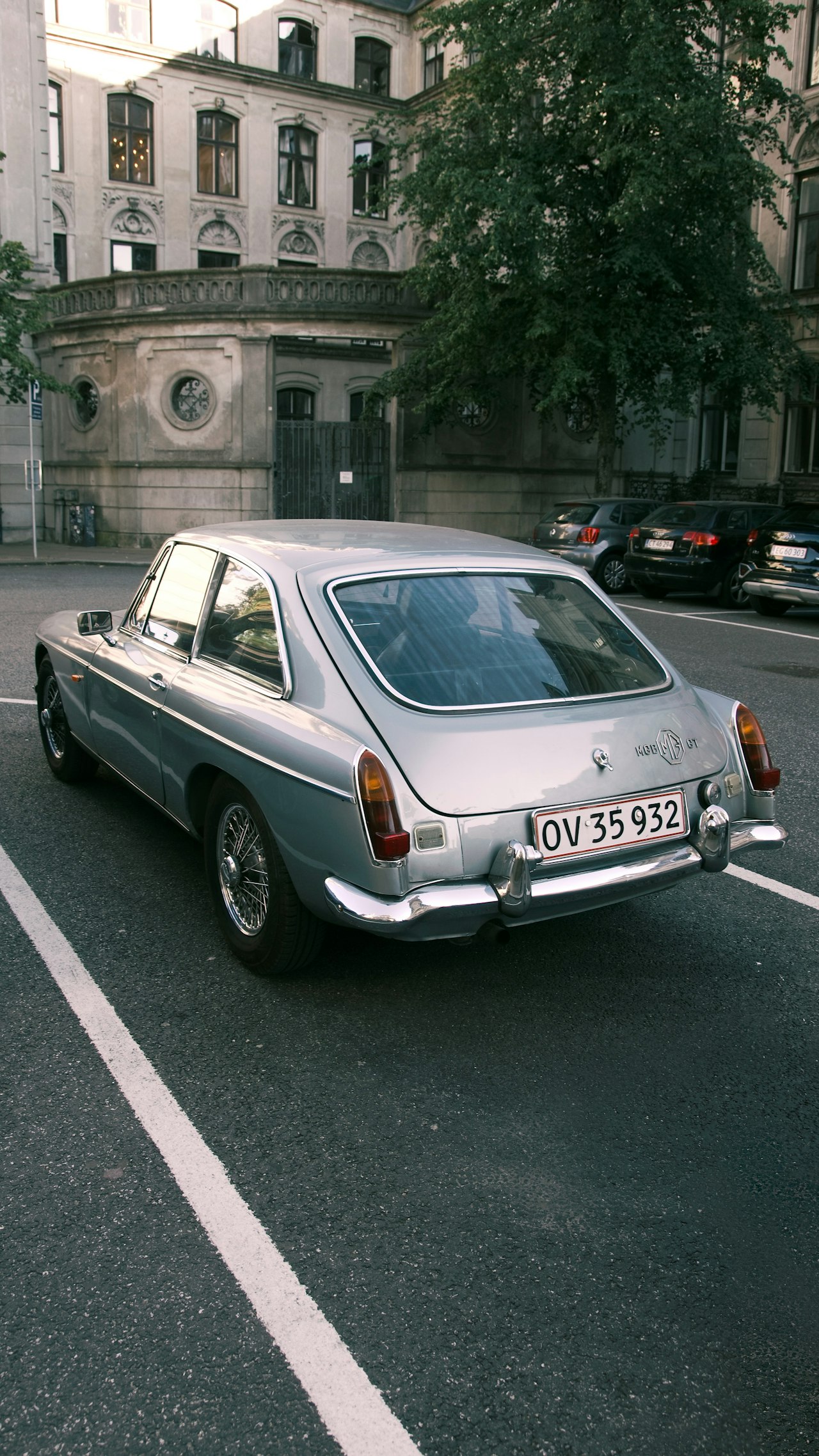 Silver MGB parked on a street, showing the classic roadster profile