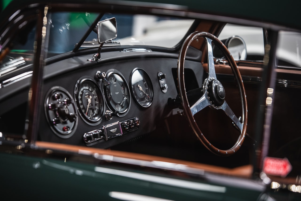 Classic British car cockpit with wooden steering wheel, chrome-ringed gauges, and black leather dashboard